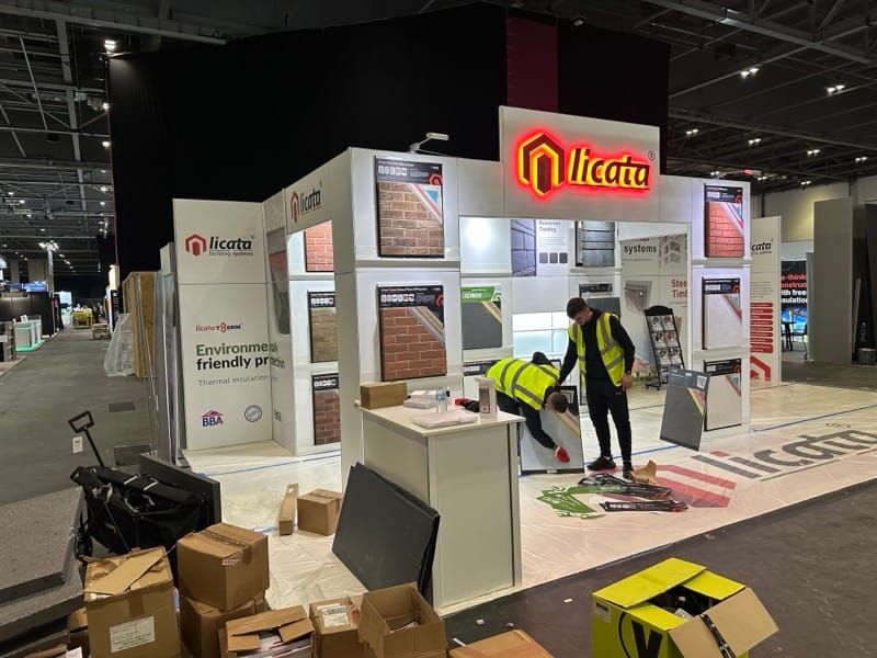 Two workers in high-visibility vests setting up an exhibition stand